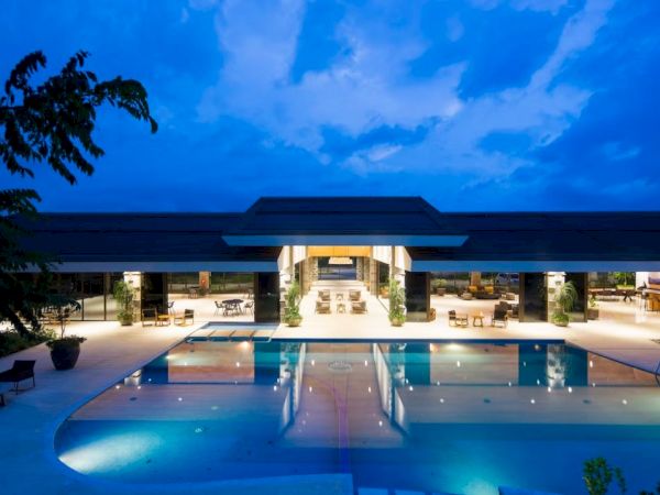 A luxurious outdoor pool area at dusk in front of a modern building with ample seating and a lit, inviting atmosphere.