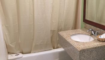 A bathroom with a shower curtain, bathtub, sink with counter, mirror, and tiled floor is shown in the image.