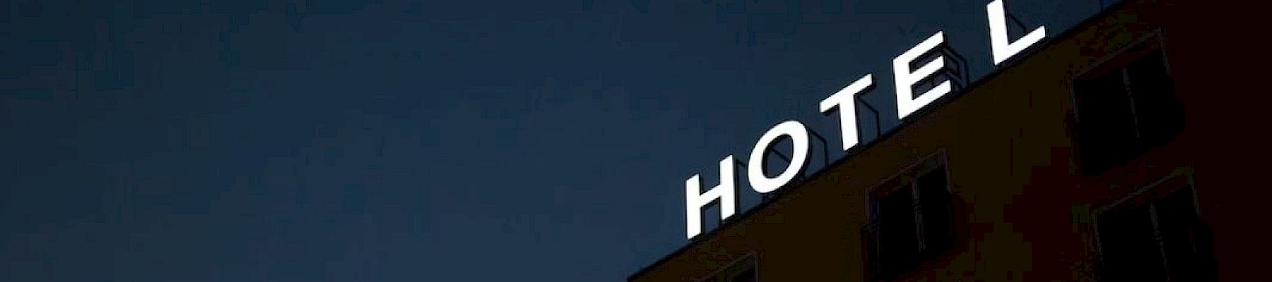The image shows a building at night with a neon sign reading "HOTEL," with the letter "L" slightly separated from the rest.