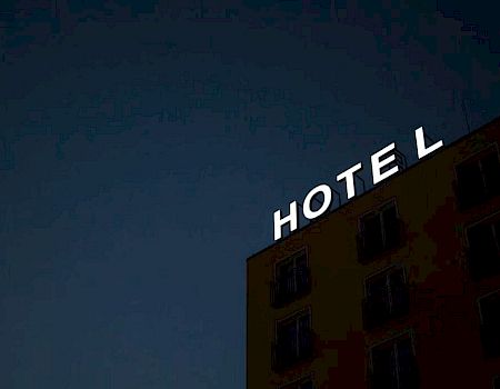The image shows a building at night with a neon sign reading "HOTEL," with the letter "L" slightly separated from the rest.