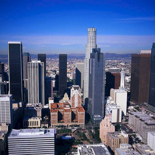 A cityscape featuring a cluster of tall skyscrapers and various office buildings under a clear blue sky. It presents an urban skyline scene.