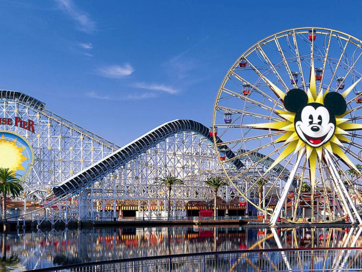 The image shows a theme park with a large Ferris wheel featuring a Mickey Mouse face, and a roller coaster with a 