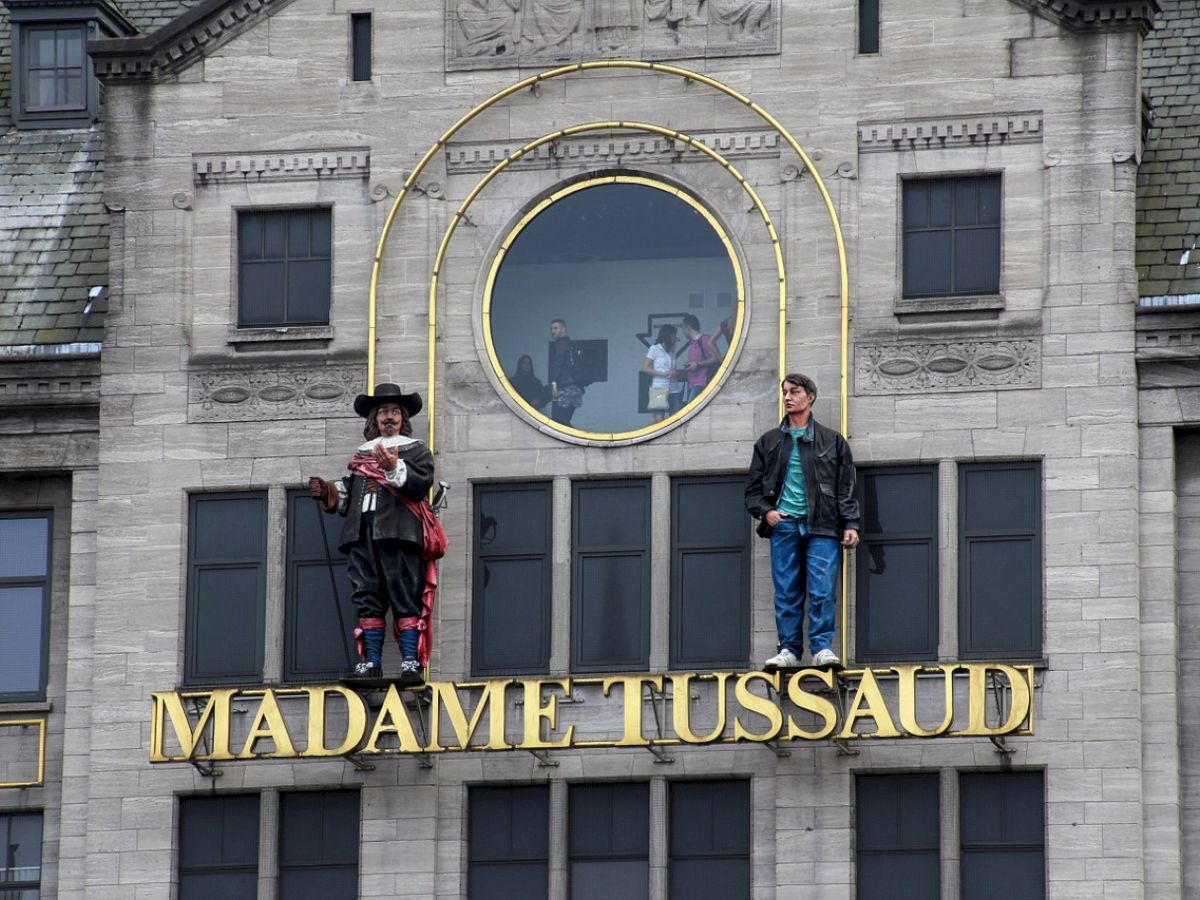 The image shows the exterior of Madame Tussaud's museum with wax figures on display above its sign.