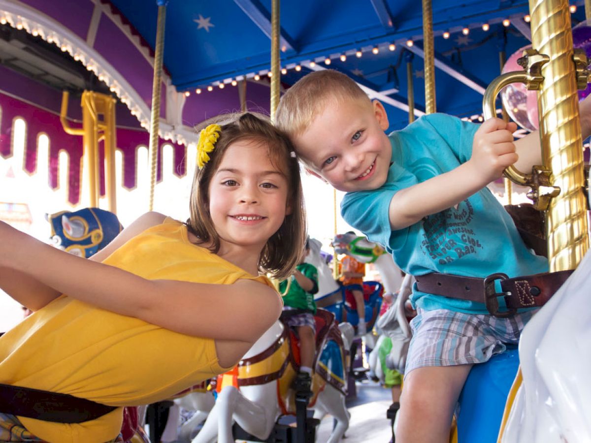 Two children smile while riding a colorful carousel, with vibrant decorations and a joyous atmosphere surrounding them.