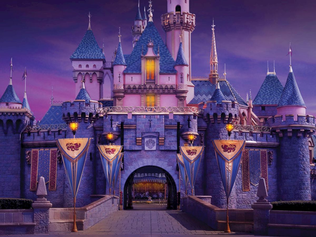 The image shows a beautifully lit castle with blue rooftops and banners, set against a dusk sky, creating a magical and enchanting atmosphere.