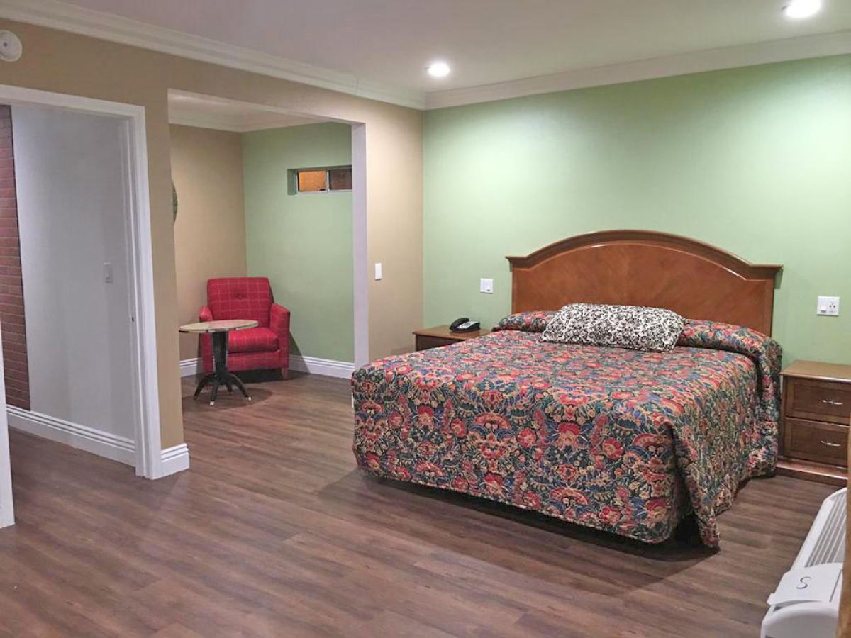 A room with a large bed adorned with a floral bedspread, a red chair with a small round table, wooden flooring, and green walls.