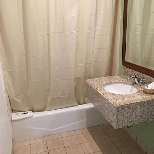 A bathroom with a shower curtain, a bathtub, a floating sink with a mirror above, and tiled flooring.