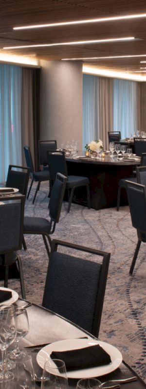 The image shows an elegantly set dining room with multiple round tables, chairs, and place settings, ready for an event or banquet.